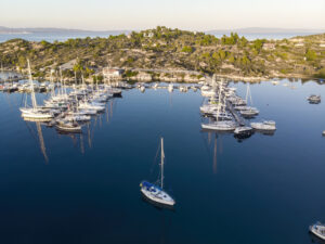 Aegean sea port with multiple moored yachts near piers, greenery, blue water, view from the drone, Greece