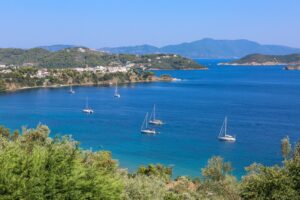 A high angle shot of sailing ships on the ocean near grassy hills in Skiathos Greece on a sunny day