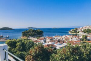 A wide shot of white and brown buildings near sea surrounded by trees and small islands in Skiathos, Greece
